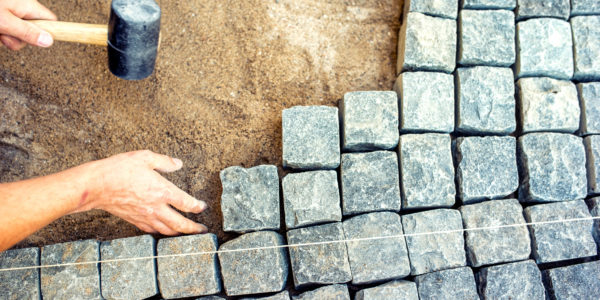 industrial worker installing pavement rocks, cobblestone blocks on road pavement